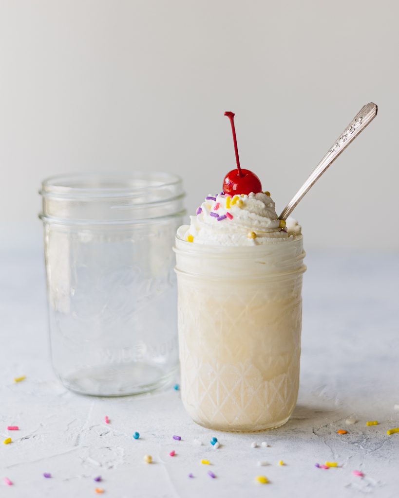 Empty mason jar and smaller mason jar filled with a vanilla milkshake and spoon.