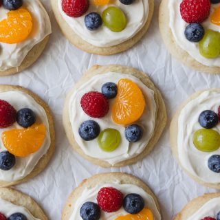 Mini fruit pizza cookies topped with cream cheese frosting and mixed fruit and berries.