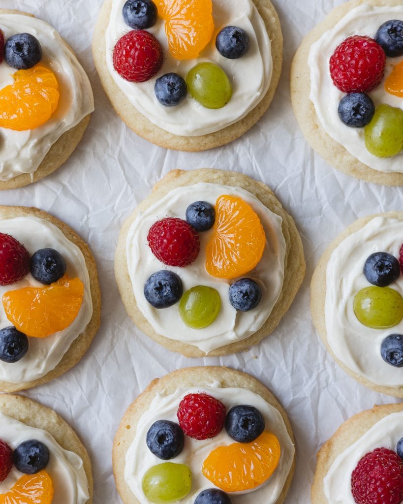 Mini fruit pizza cookies topped with cream cheese frosting and mixed fruit and berries.