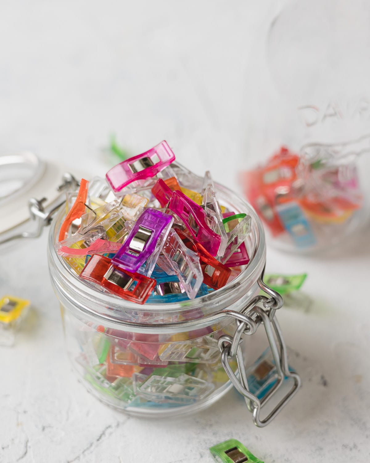 A glass jar filled with colorful quilting clips for sewing.