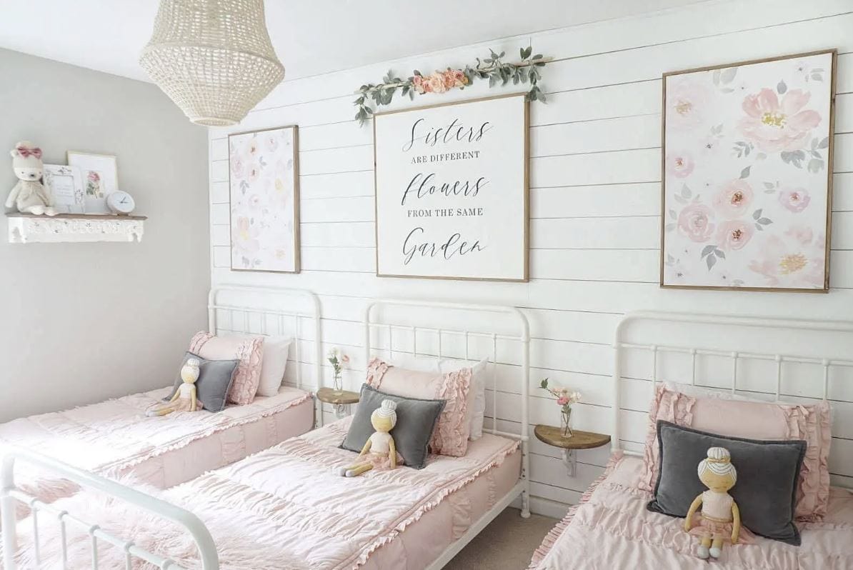 A bedroom for three sisters with three white beds with pink bedding and floral prints and accents.