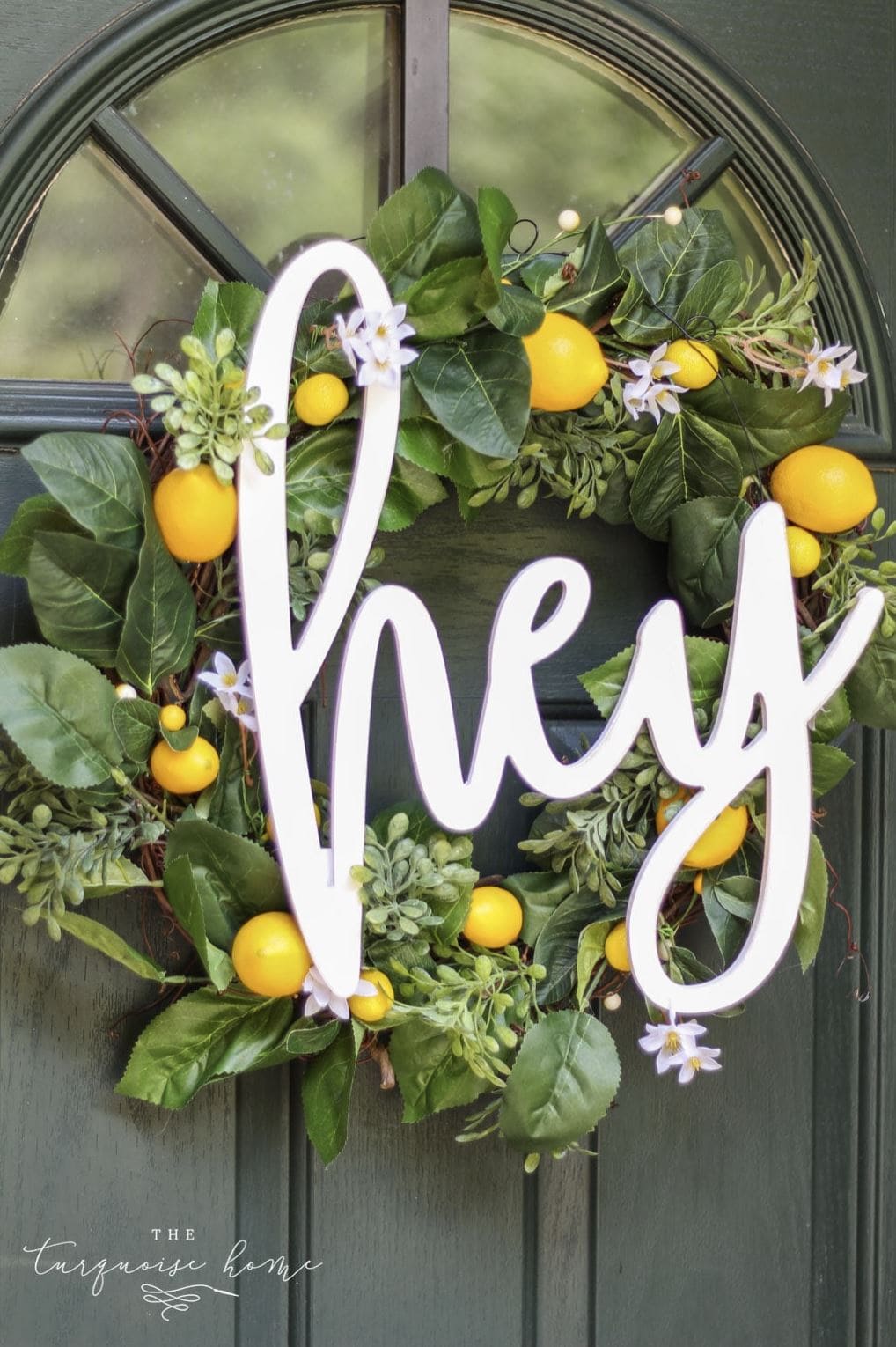 A DIY lemon wreath with a wooden word cutout reading "Hey" on a front door.