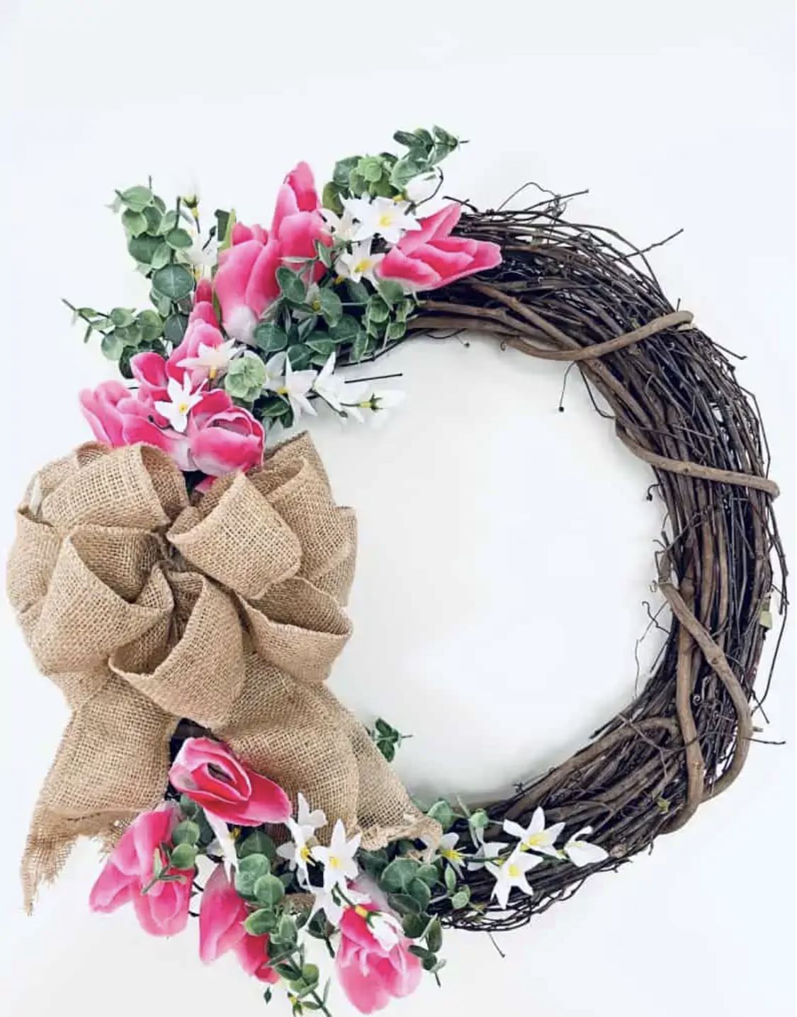 A grapevine wreath with a burlap bow and pink flowers.