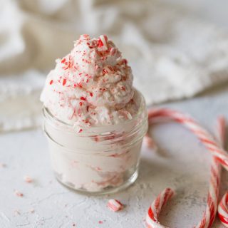 A small mason jar filled with peppermint candy whipped cream, pieces of candy canes, and whole candy canes surrounding.
