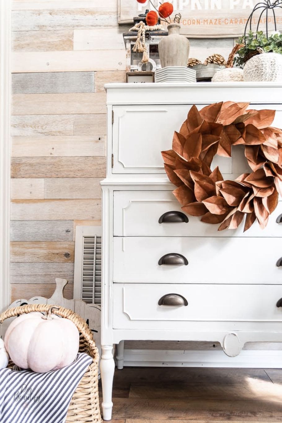 A copper magnolia leaf wreath hanging on a white painted dresser.