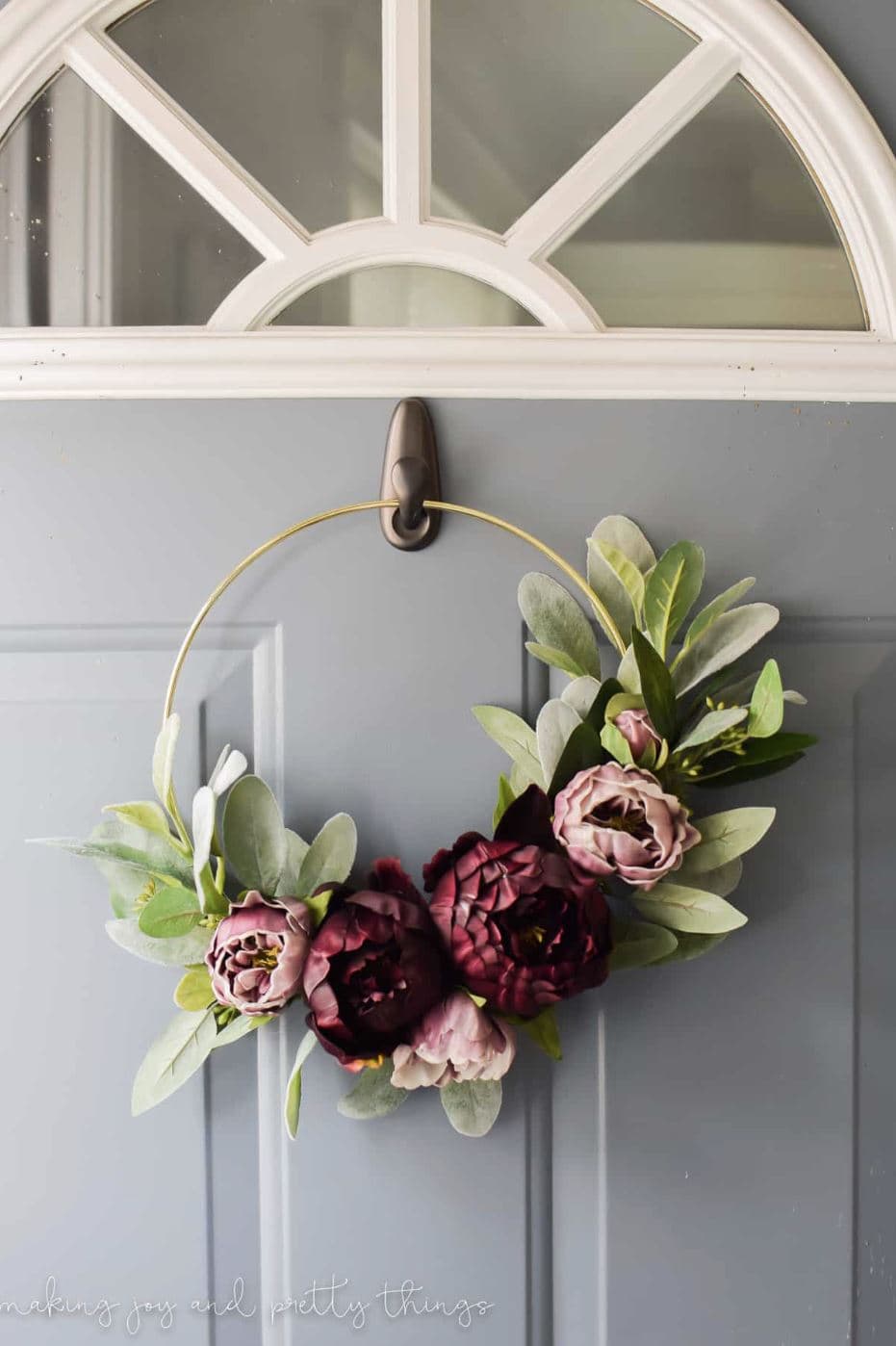 An embroidery hoop wreath with mauve and burgundy florals hanging on a front door.