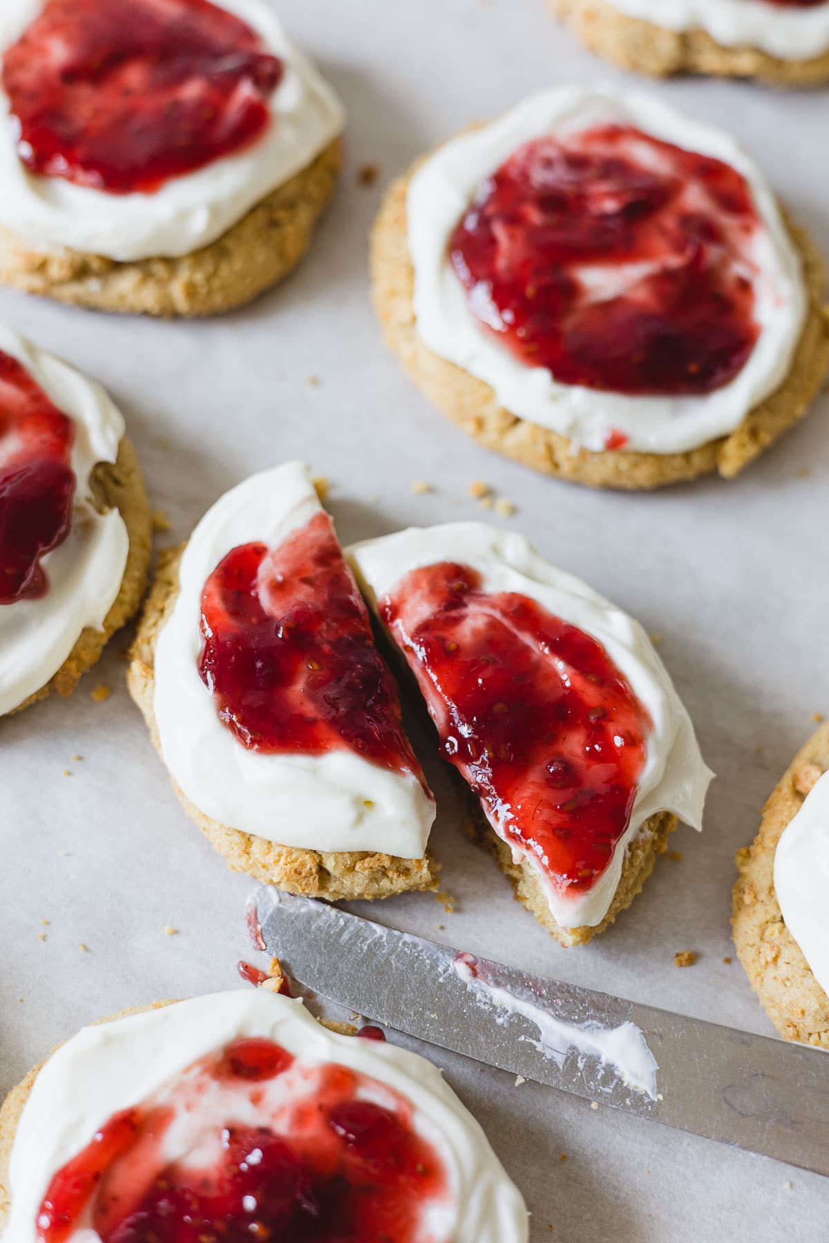 A cookie frosted with a cream cheese topping and raspberry jam cut down the middle with a butter knife.