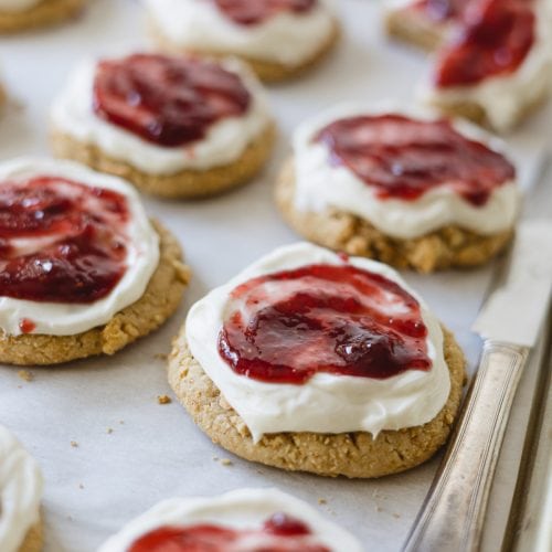 Raspberry Cheesecake Cookies with frosting and raspberry jam on a baking tray.
