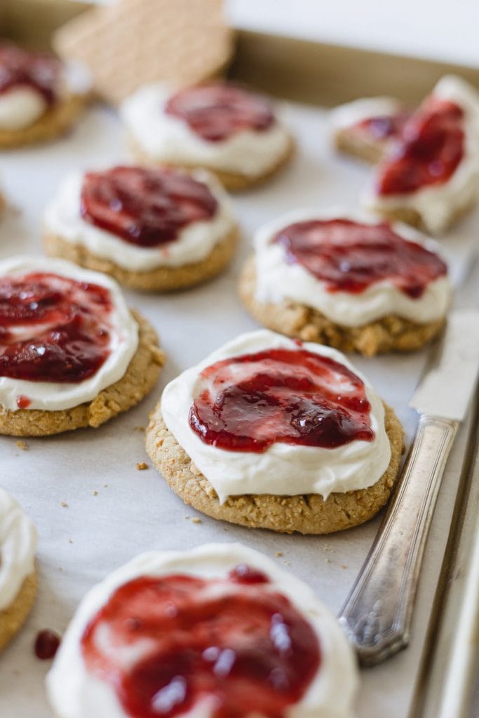 Raspberry Cheesecake Cookies with frosting and raspberry jam on a baking tray.