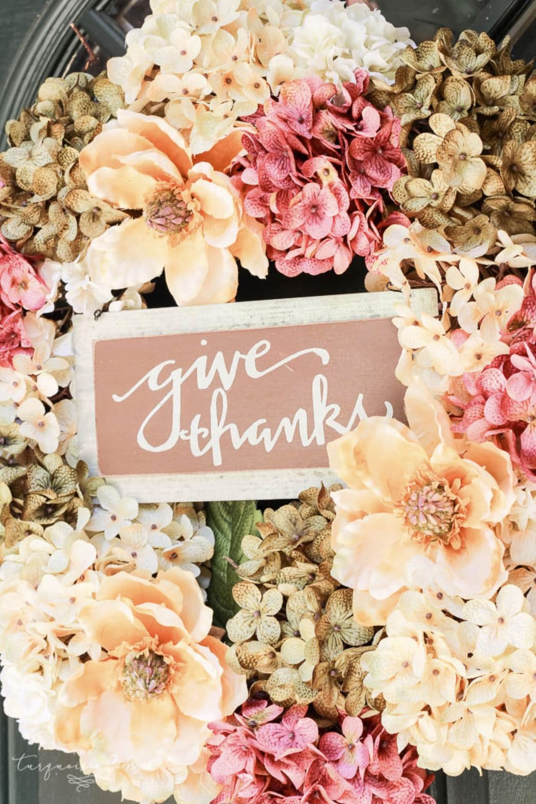 A fall floral wreath with a small wooden sign reading, "give thanks" in cursive font.
