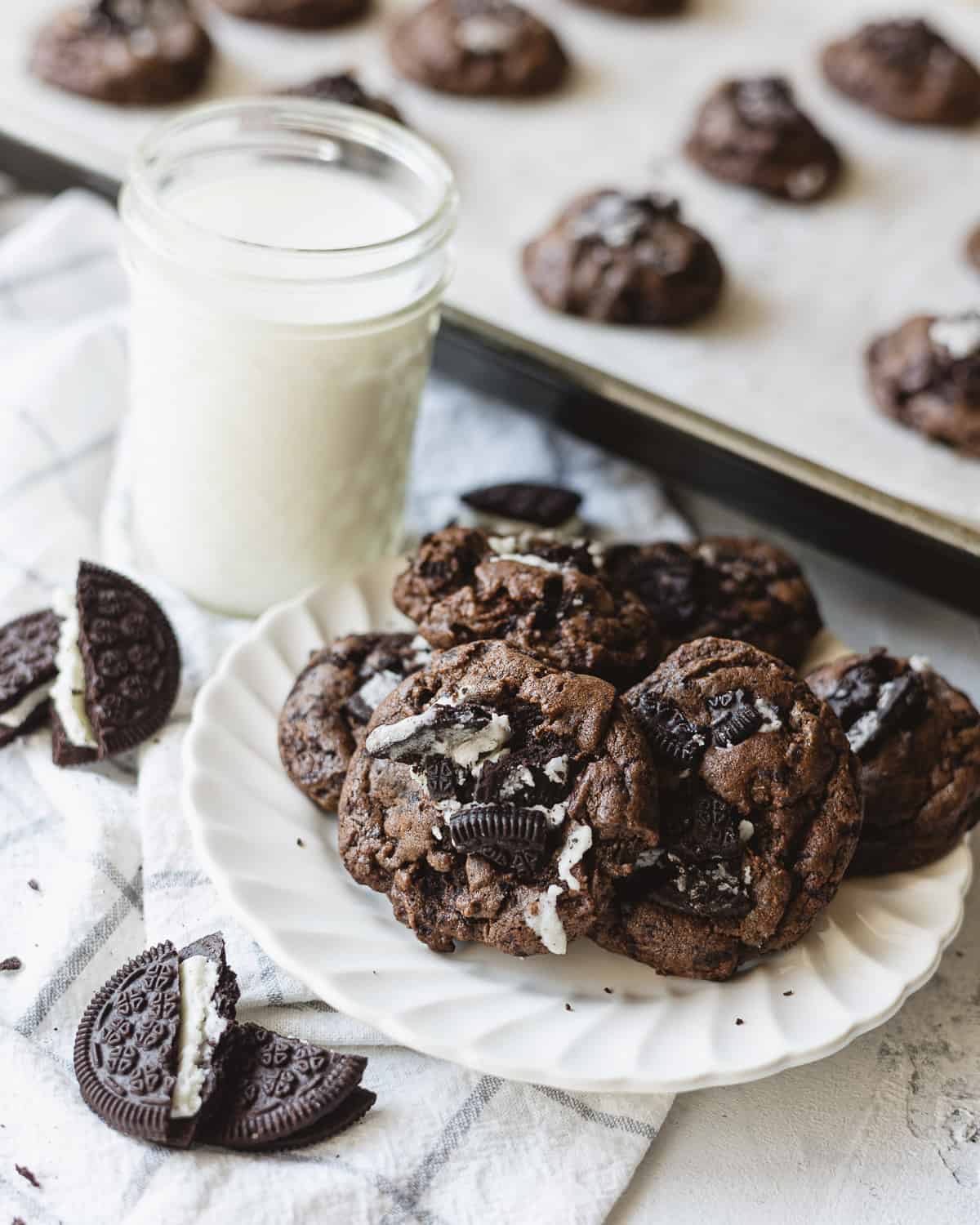A plate of chocolate cookies, a glass of milk, and broken chocolate sandwich cookies.