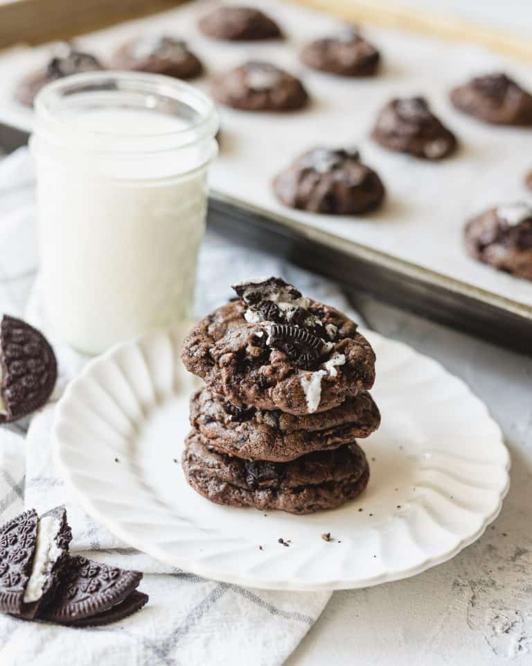 A stack of cookies with crushed oreos baked into the tops on a white scalloped plate.