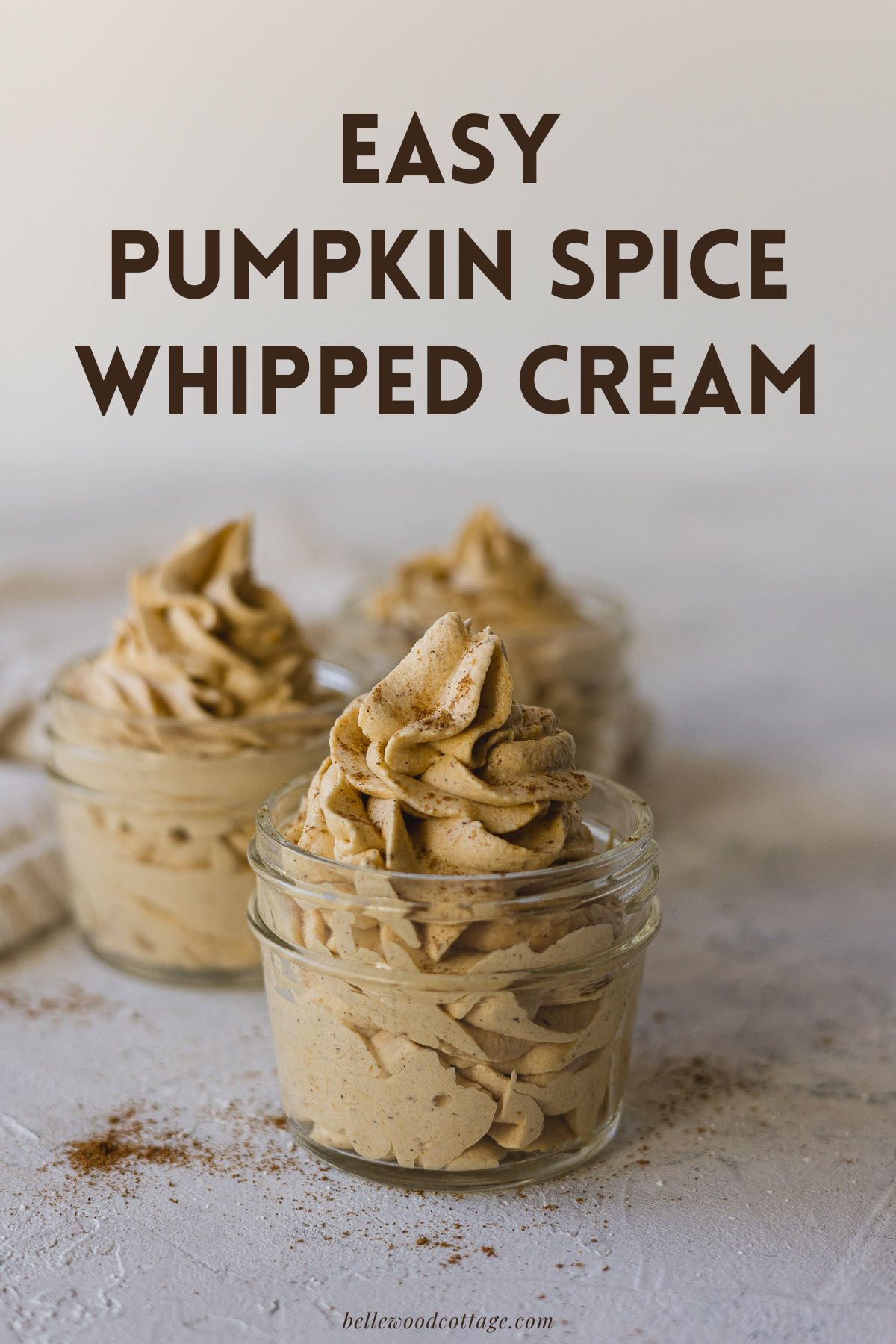 Whipped Cream sprinkled with cinnamon in mason jars with the words, "Easy Pumpkin Spice Whipped Cream."