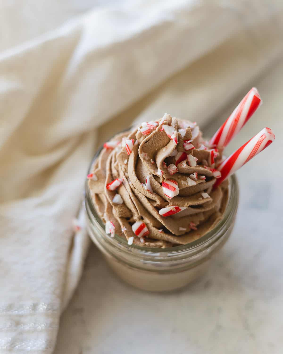 A jar of piped chocolate peppermint whipped cream with chunks of candy canes.