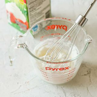 A small whisk in a measuring cup of whipped cream.