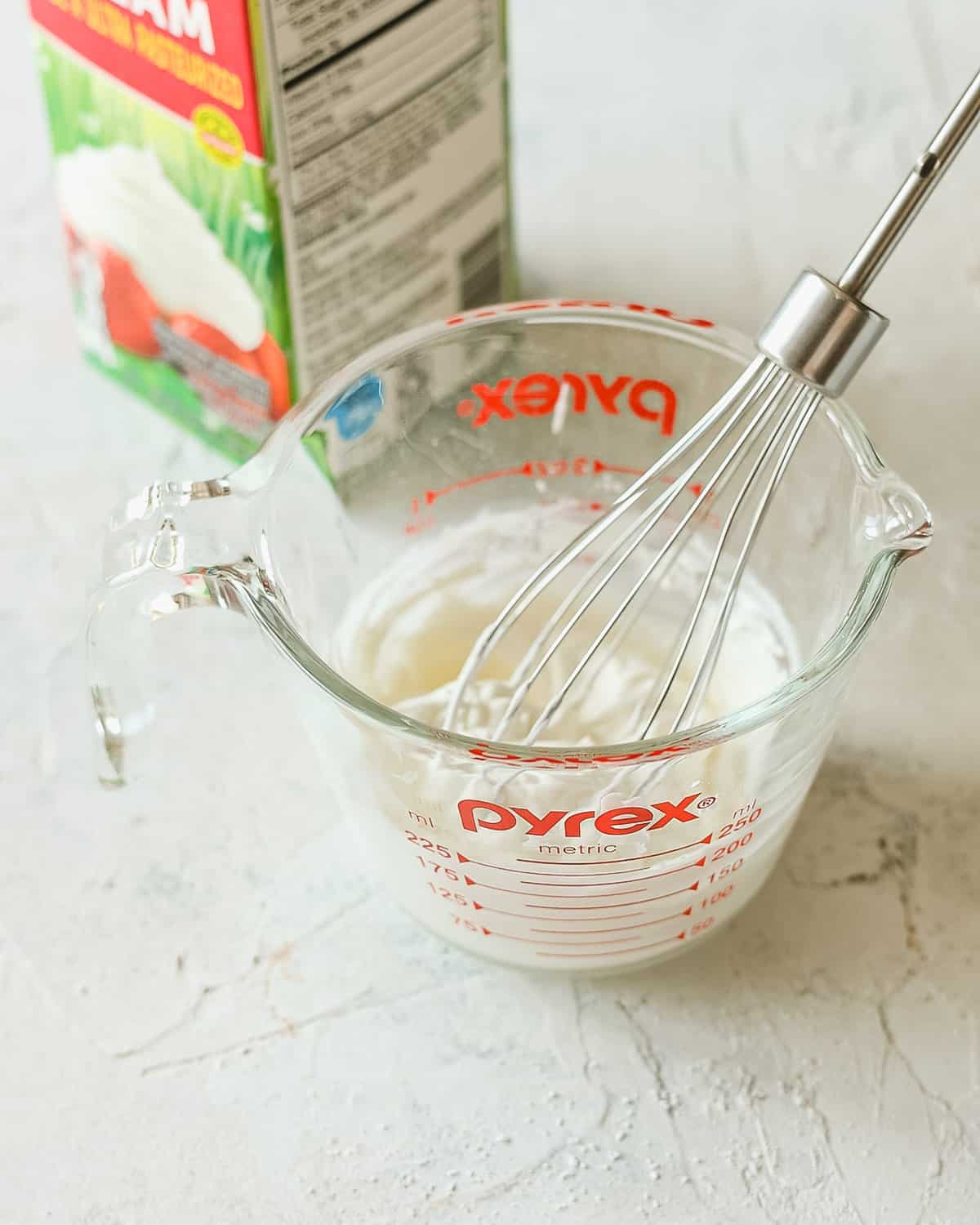 A small whisk in a measuring cup of whipped cream.