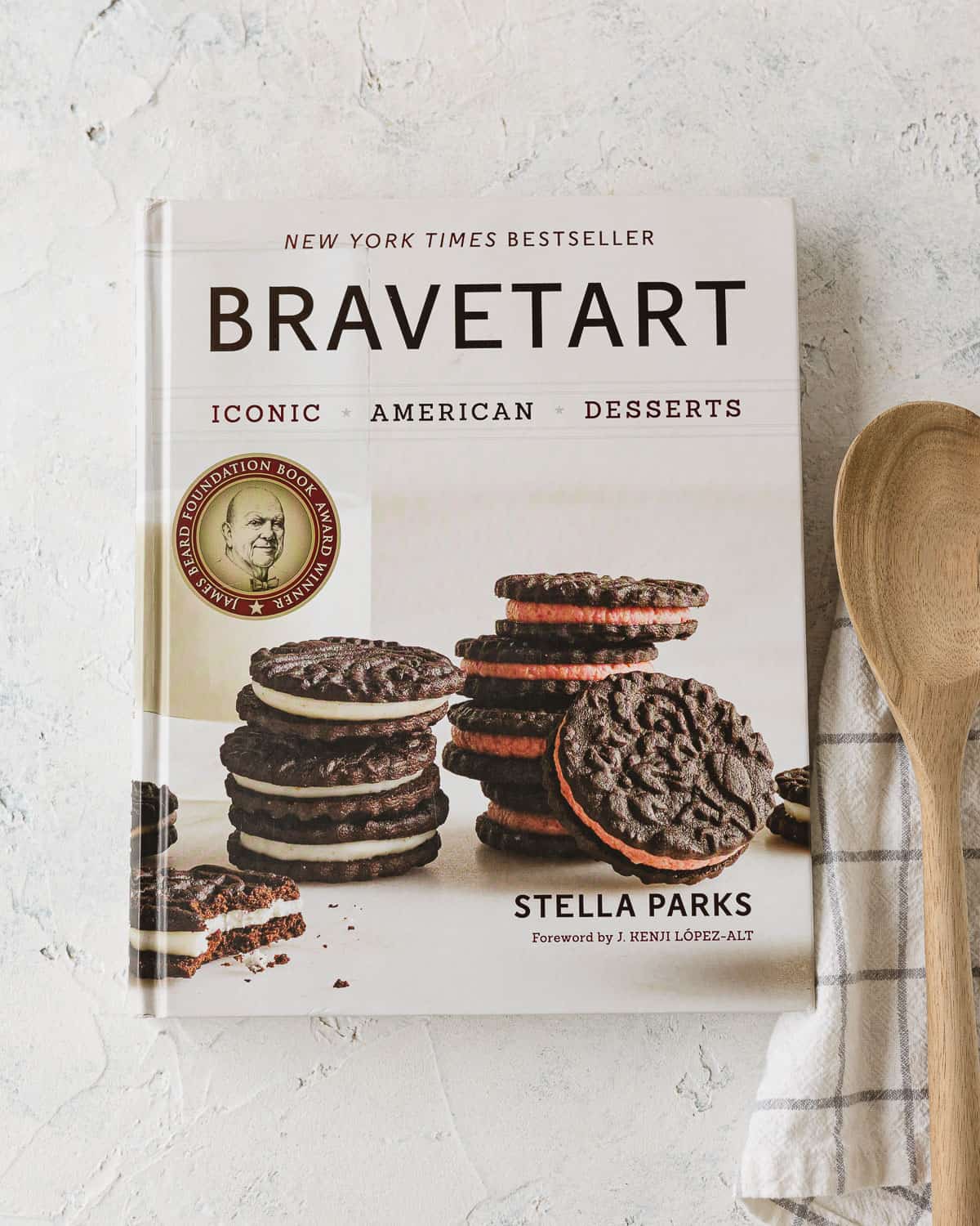 "BraveTart" book on a rustic surface with a towel and wooden spoon.
