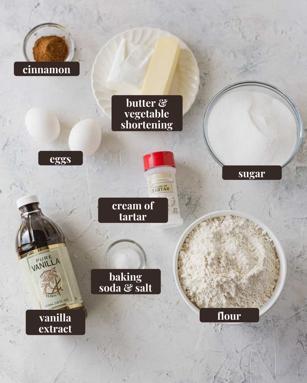 Labeled ingredients for Giant Crumbl Snickerdoodle Cookies: flour, baking soda & salt, vanilla extract, cream of tartar, eggs, cinnamon, butter and vegetable shortening, and sugar.