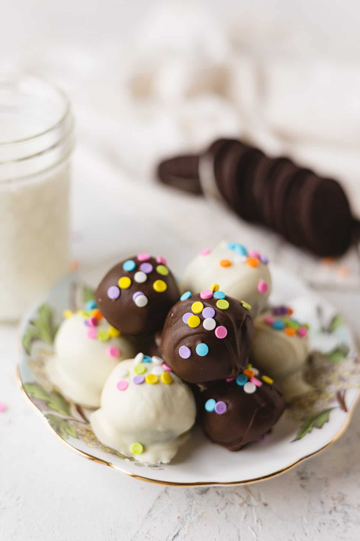 Chocolate and white chocolate Oreo Truffles decorated with confetti sprinkles on a floral plate.