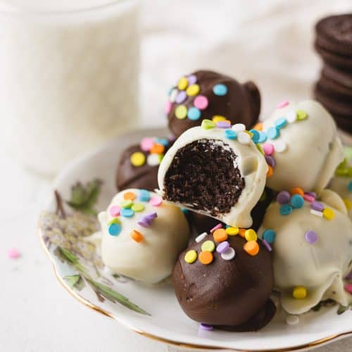 Oreo truffles coated in white and dark chocolate, decorated with sprinkles, and arranged on a floral plate.