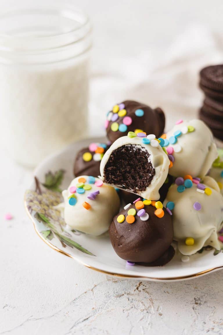 Oreo truffles coated in white and dark chocolate, decorated with sprinkles, and arranged on a floral plate.