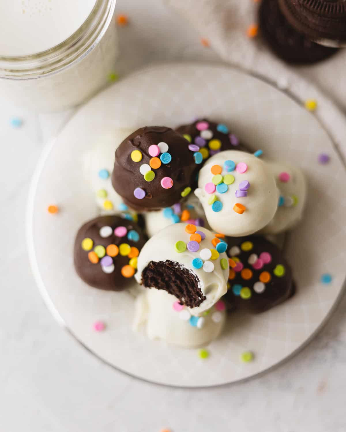 Oreo balls decorated with colorful sprinkles and arranged on a plate, one with a bite removed.