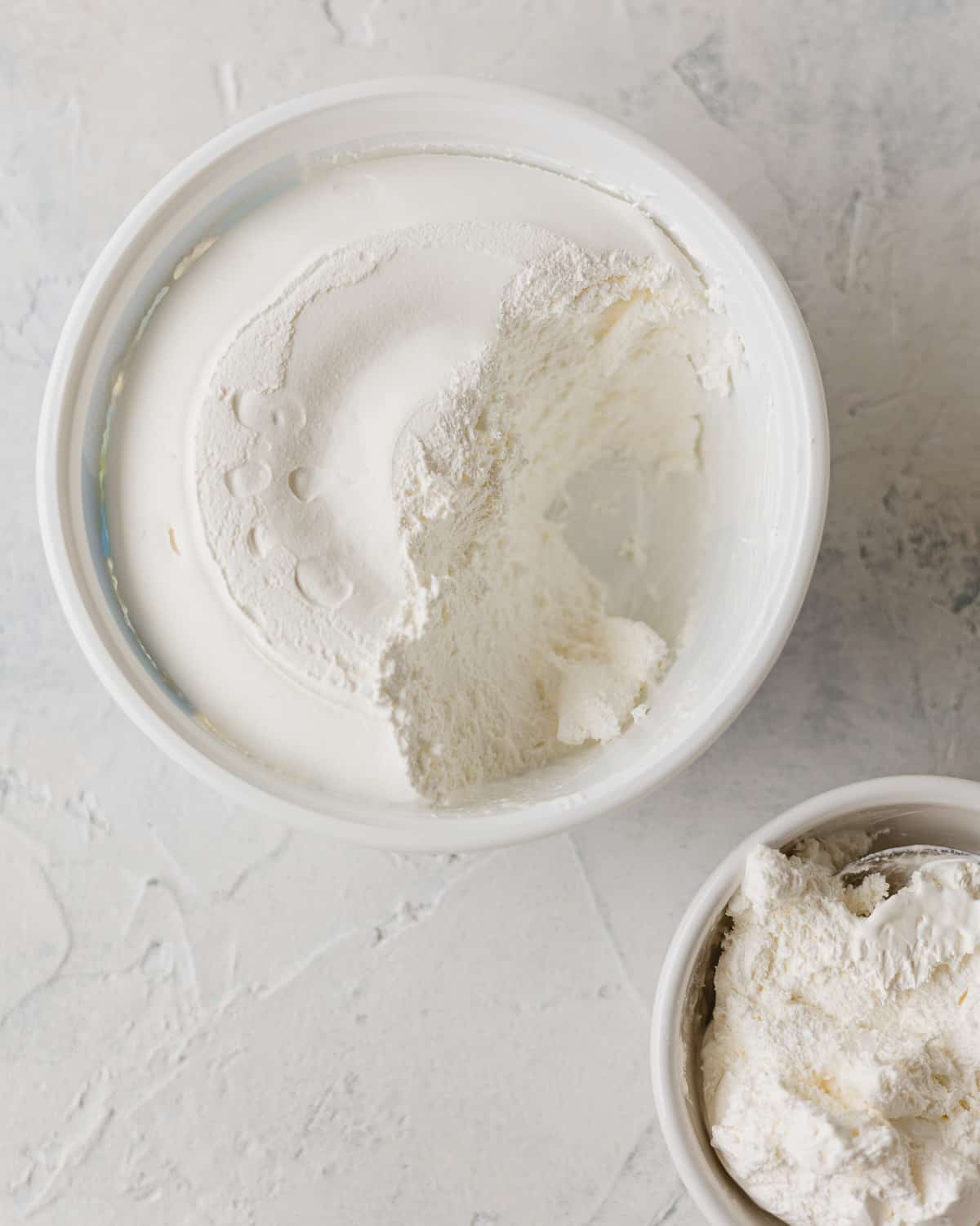 A container of Cool Whip with some removed and placed in a white bowl to the side.