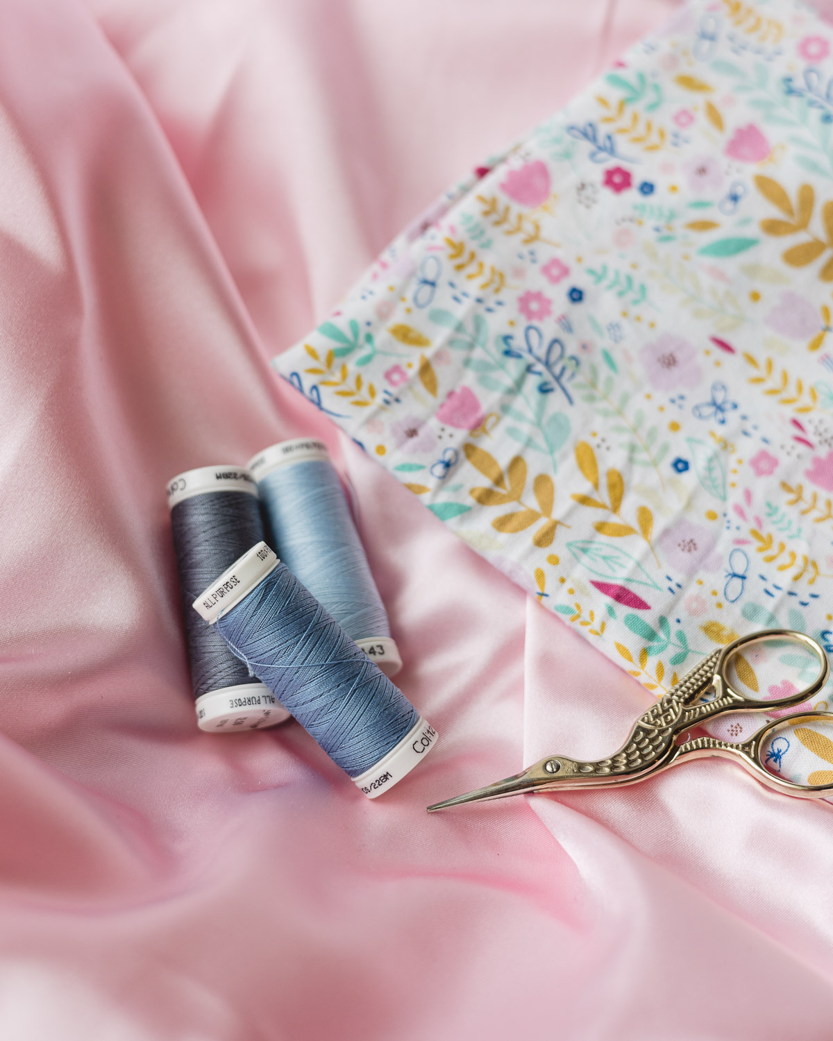 Pink fabric with three spools of blue thread and gold embroidery scissors.