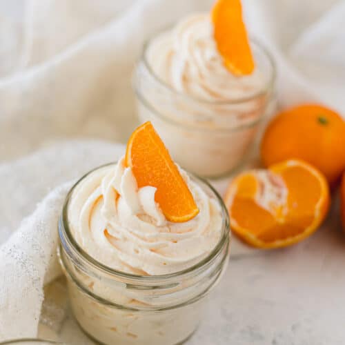 Piped orange whipped cream in mason jars with orange slices on top.