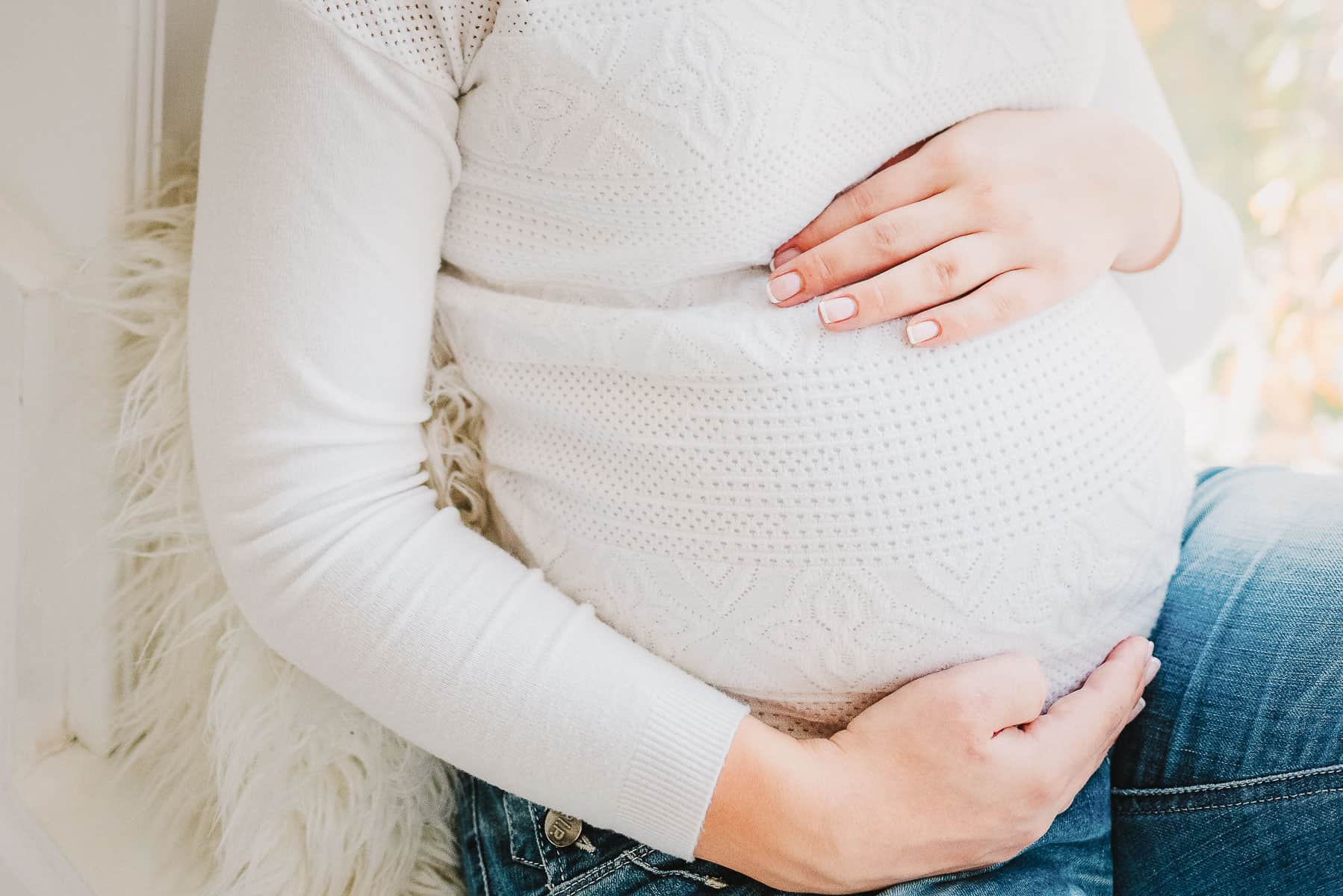 Woman in white shirt and jeans cradling a pregnant belly.