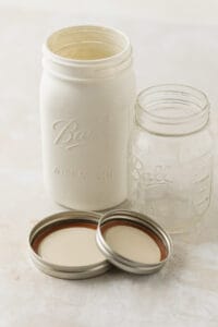 A painted wide mouth 32 ounce mason jar and a regular mouth 16 ounce jar with lids.
