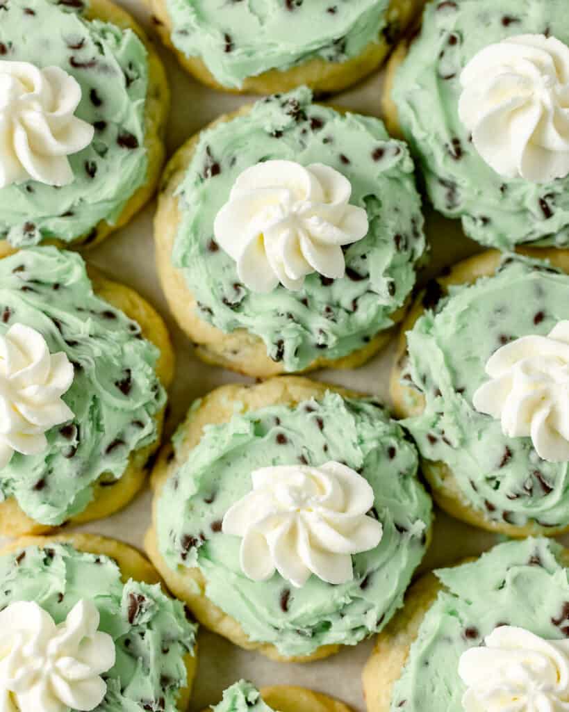 Sugar cookies frosted with green mint chocolate chip frosting and a piped rosette of whipped cream.