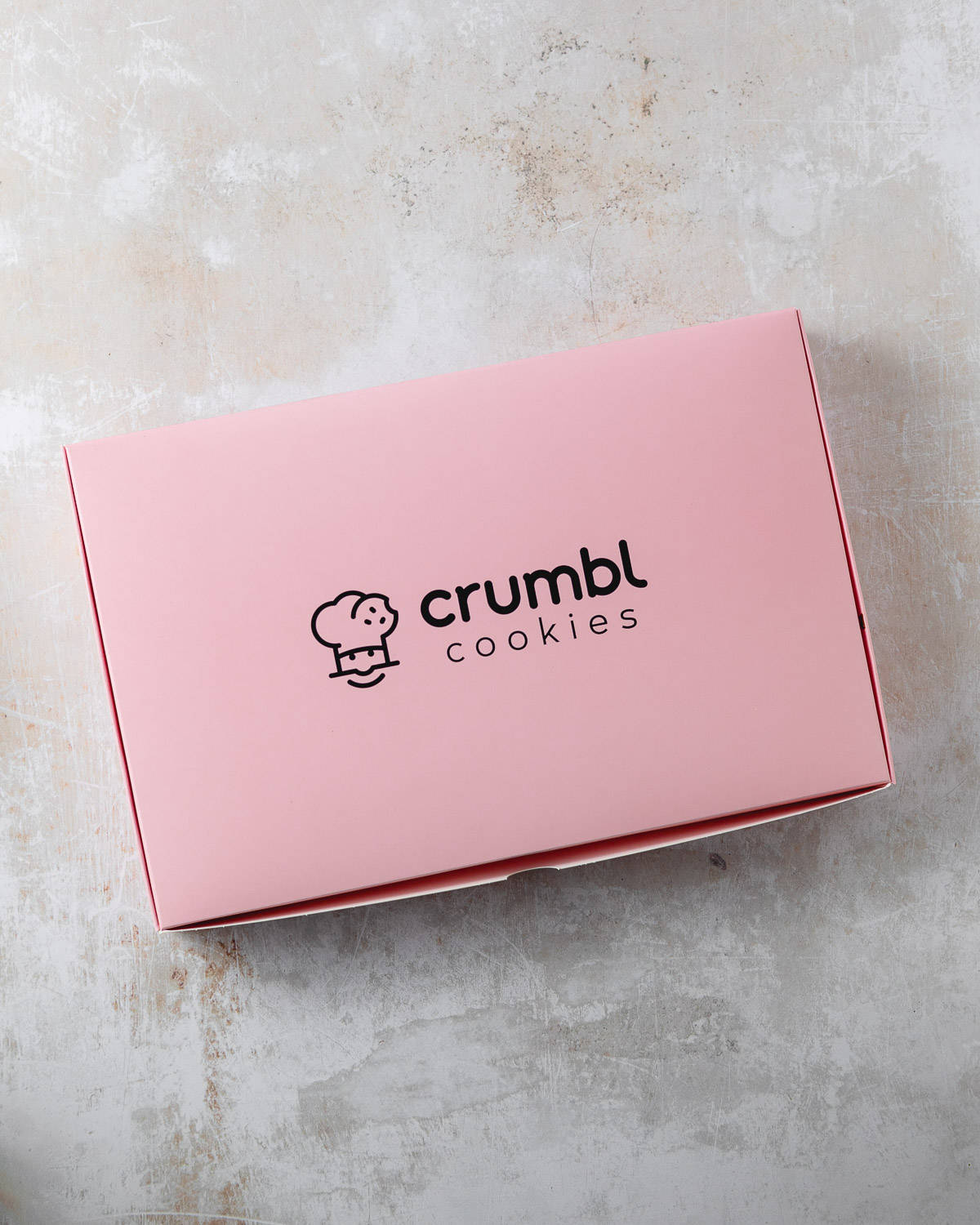 A pink Crumbl Cookies 6-pack box on a rustic surface.