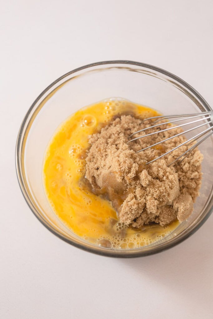 A whisk in a bowl of sugar and eggs.