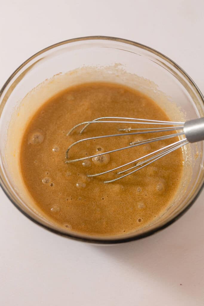 A whisk in a bowl of blended eggs and sugar.
