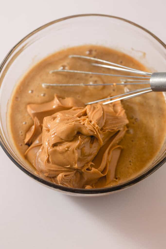 Peanut butter being whisked into a mixture of eggs and sugar.