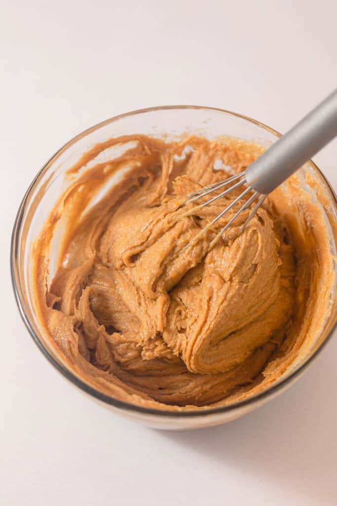 Whisking a thick peanut butter dough in a glass bowl.