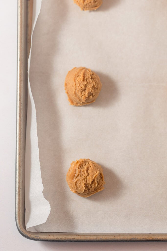 Scooped peanut butter cookies on a lined baking pan.