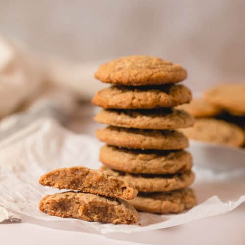 A large stack of peanut butter cookies with one broken in half with the halves stacked.