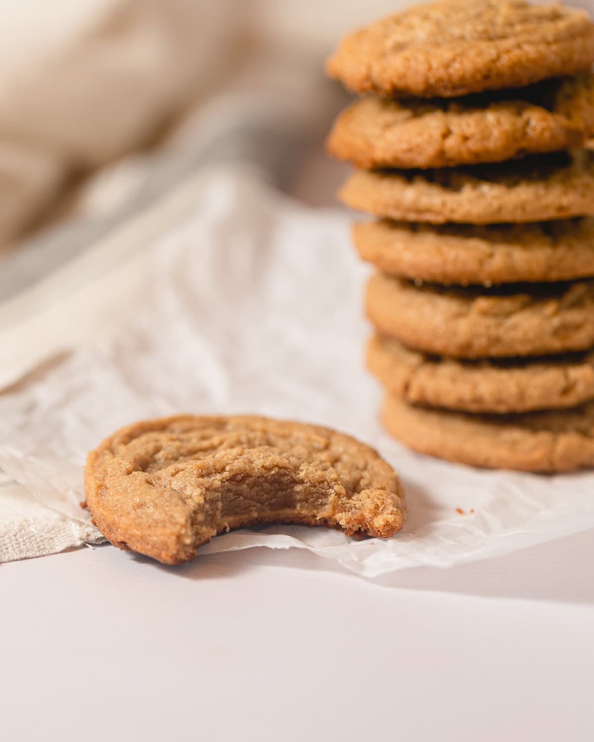 A stack of peanut butter cookies with a single peanut butter cookie with a bite removed.