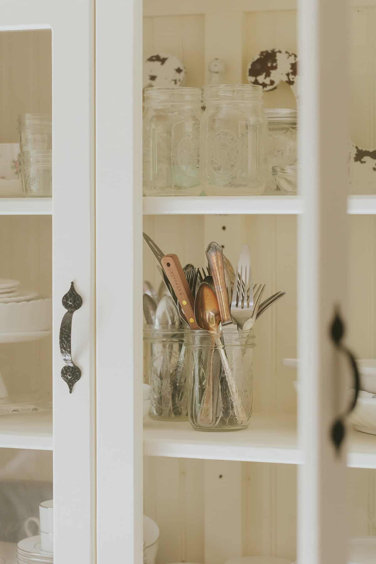 Dishes and flatware arranged in a hutch with glass doors.
