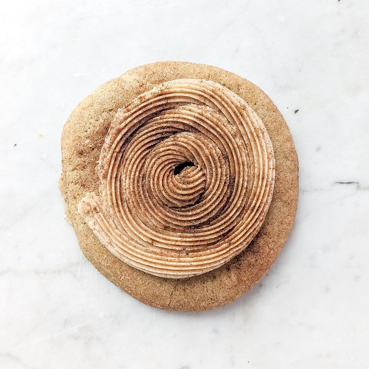 A Crumbl Cookies Churro cookie with a swirl of frosting topped with cinnamon sugar.