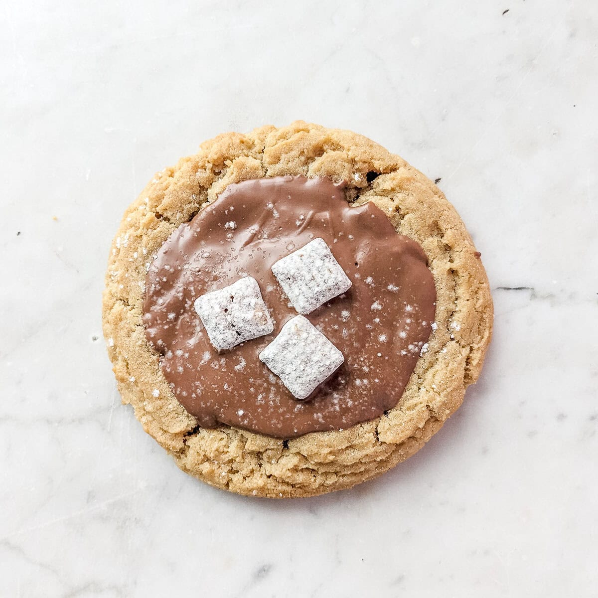 A peanut butter crumbl cookie with milk chocolate and Muddy Buddies on top.