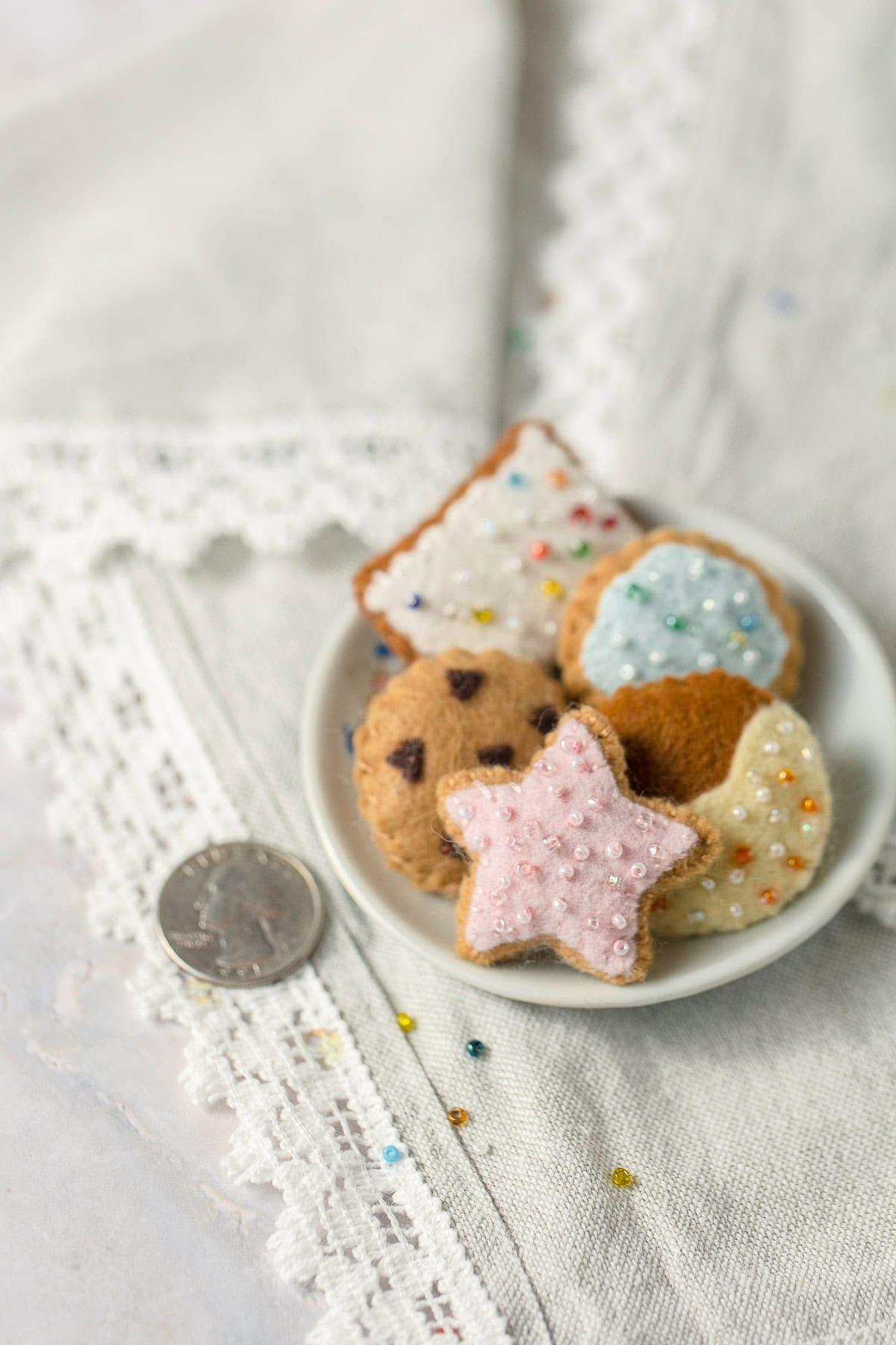 A quarter for scale alongside a mini plate of felt cookies decorated with seed beads.