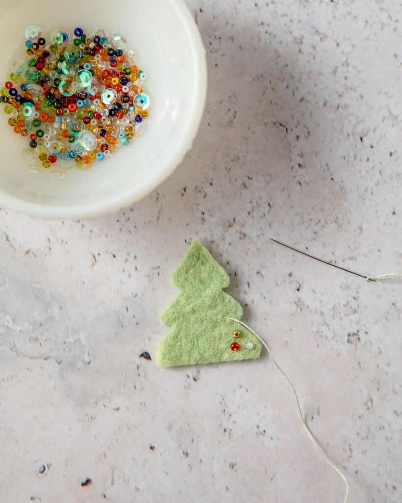 Stitching seed beads onto a tiny tree-shaped piece of green felt.