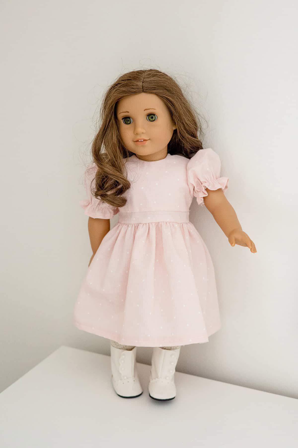 American Girl "Rebecca" doll dressed in a handmade pink dress with puffed sleeves, white tights, and white button-up boots.