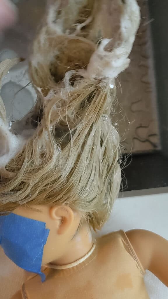 Washing doll hair over a stainless steel sink.